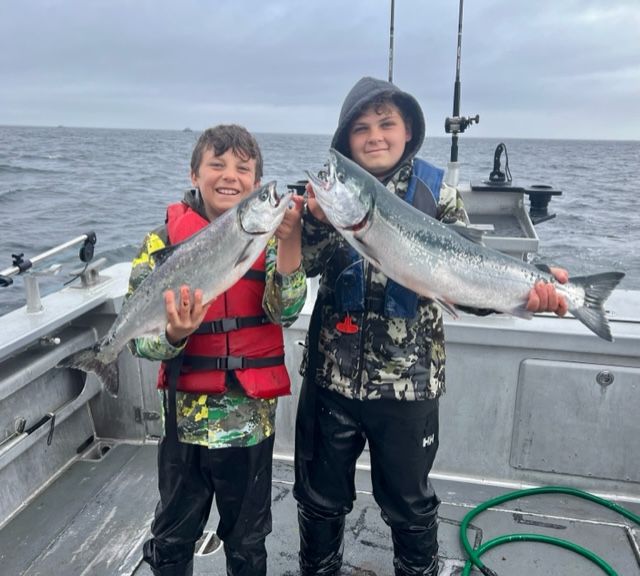 Two kids on a fishing boat holding two fishes