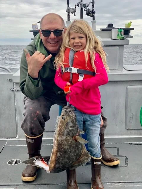 A man and girl holding fish on the deck of boat.