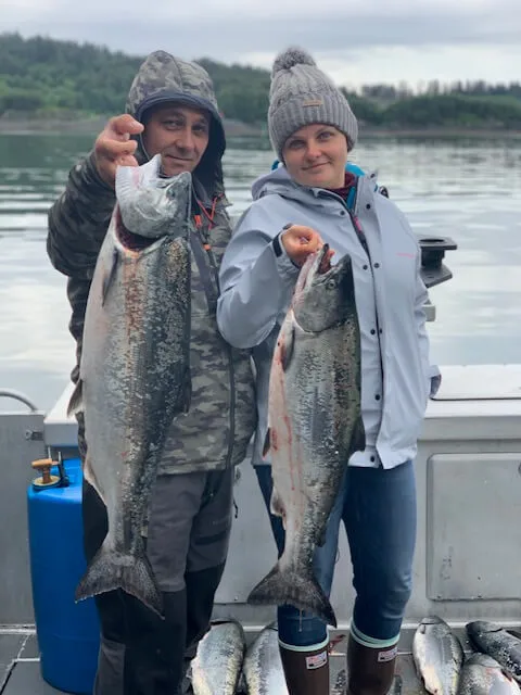 Two people holding up fish on a boat.