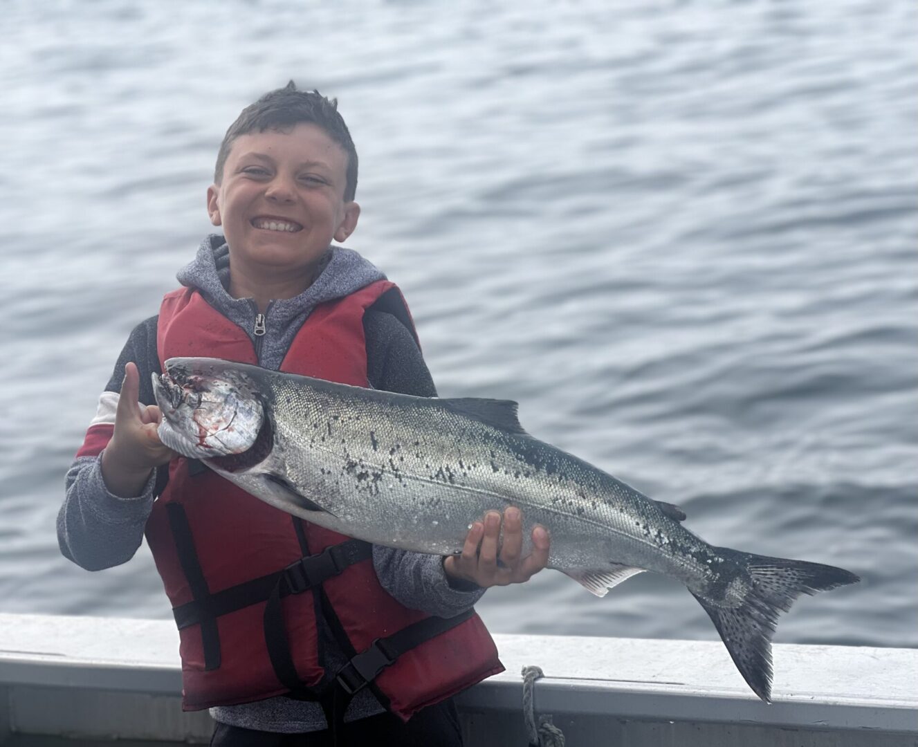 A kid holding a bog fish on a boat and smiling,